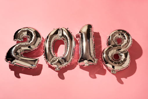 some silvery number-shaped balloons forming the number 2018, as the new year, against a pink background