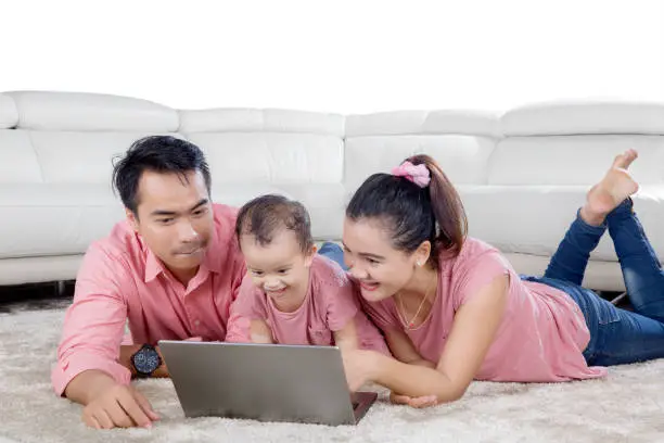 Image of happy family playing with a laptop while lying together on the carpet