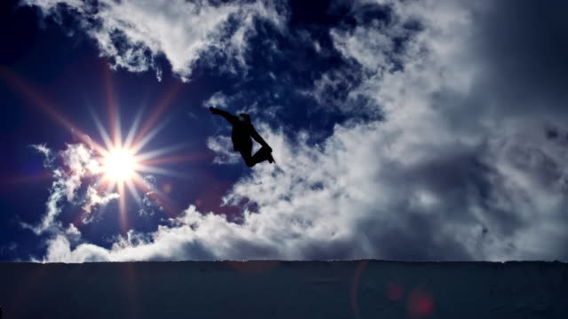 SLO MO LD Snowboarder airborne in the half-pipe with sun in the background