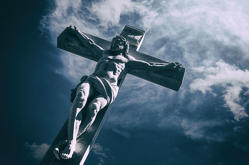 A sculpture of Jesus Christ on the cross against a dramatic sky.