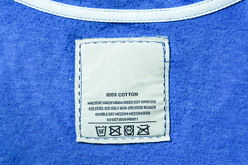 Clothing label with laundry instructions, close-up of person reading the clothing label showing washing Instructions,clothes, housekeeping concept.