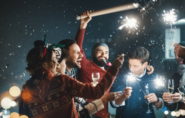 New Year's rooftop party. Closeup of group of mixed age people having New year's party at a building rooftop. They are having champagne, lighting up some fire sparklers and popping confetti. firework display pyrotechnics celebration excitement stock pictures, royalty-free photos & images