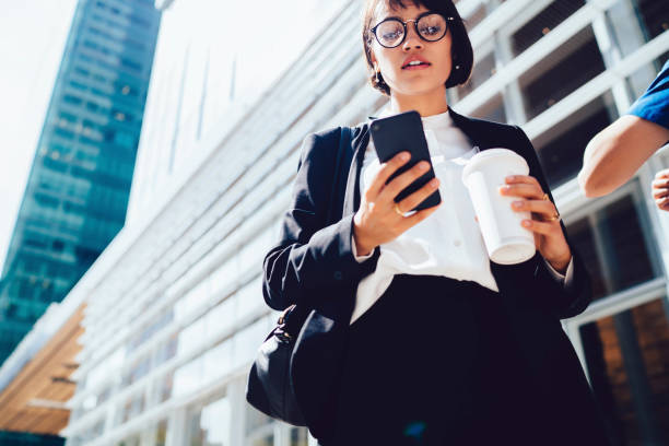 istock Serious female director reading message on mobile while walking in business district holding coffee to go cup with copy space for brand name or label, confident owner checking mail on city street 897391532