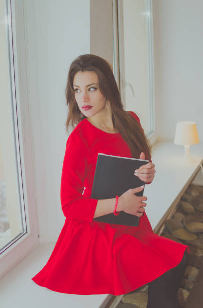 istock girl in red at a window with a book 897399354