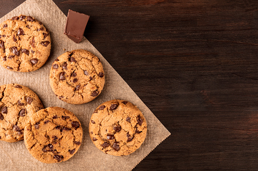 An overhead photo of chocolate chips cookies with a slice of chocolate, shot from above on a piece of baking paper, with copy space