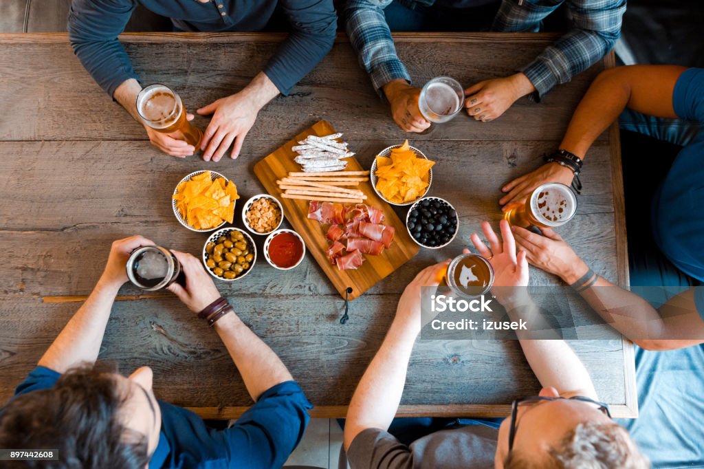 Top view of friends sitting over beer at the table in pub Top view of friends sitting at the table in the pub, drinking beer. Unrecognizable people. High angle view of table. Snack Stock Photo