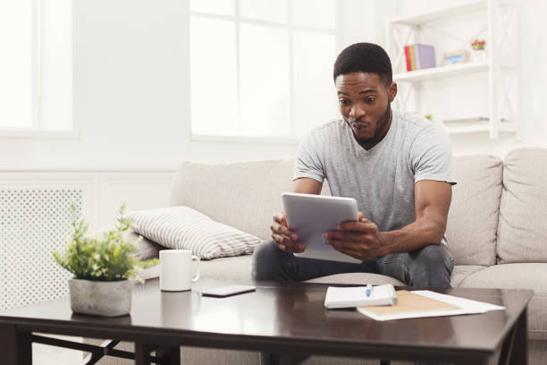 istock Surprised young man at home reading on tablet 897492774