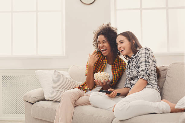 Smiling young women watching TV at home Smiling young women relaxing and watching TV at home, female friends having rest after hard week, copy space emotional series stock pictures, royalty-free photos & images