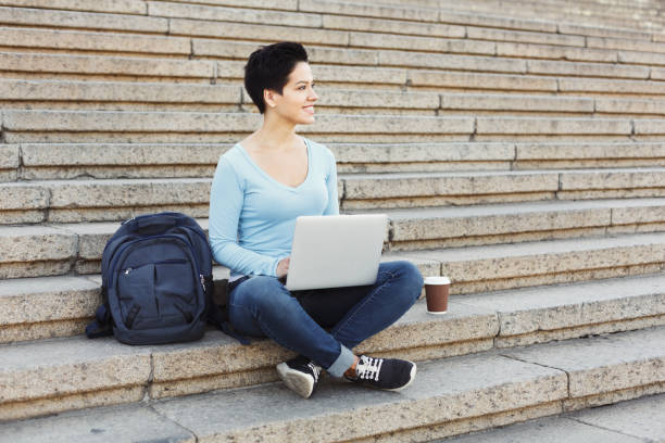 istock Smiling woman sitting on stairs using laptop 897512644