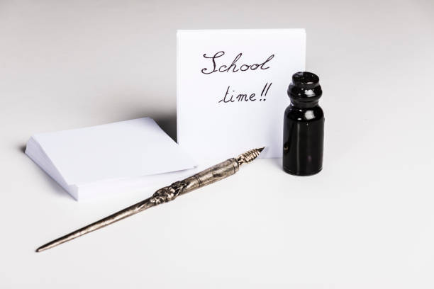 An old pen with a small bottle of ink are in front of a note where is written School time!!