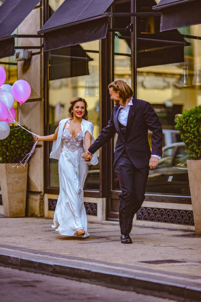 istock Affectionate bride and groom, holding hands, happily run down the street 897553668