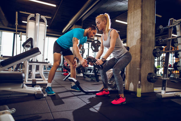 Young woman lifting weights with help of personal trainer Young woman lifting weights with the assistance of her personal trainer at the gym. Barbell stock pictures, royalty-free photos & images