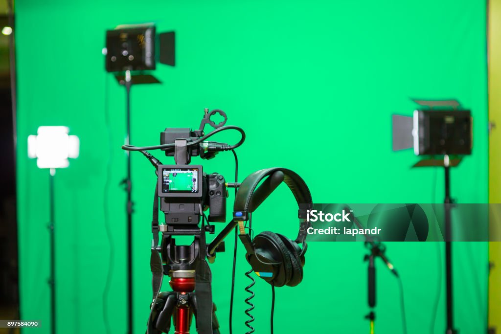 La cámara en el trípode, reflector led, auriculares y un micrófono direccional en un fondo verde. La clave de croma. Pantalla verde - Foto de stock de Cámara de vídeo libre de derechos