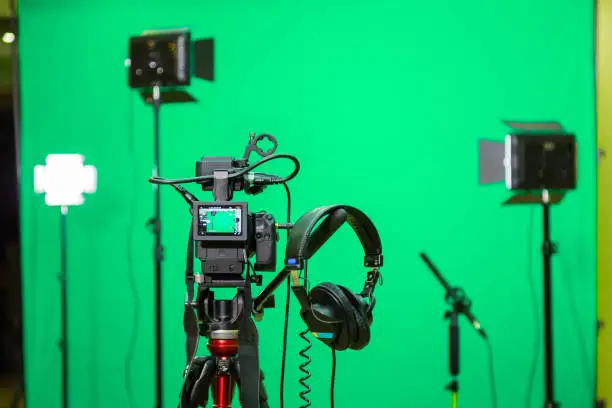 Photo of The camera on the tripod, led floodlight, headphones and a directional microphone on a green background. The chroma key. Green screen