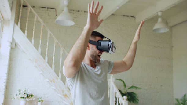 istock Cheerful young man have fun and dance while getting experience using 360 VR headset glasses of virtual reality in bedroom at home 897584346