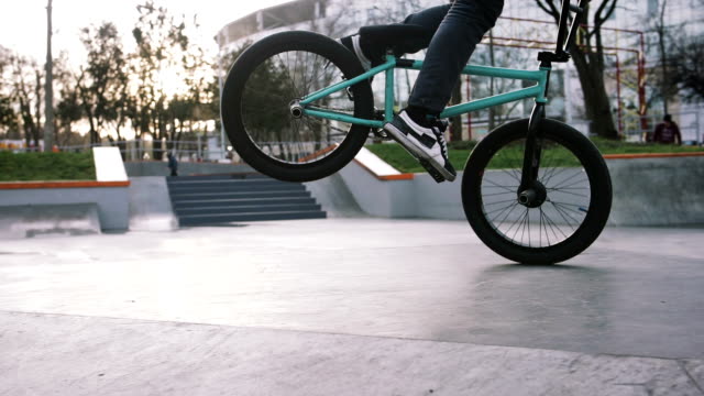 BMX rider doing tricks in street plaza, bicycle stunt rider in cocncrete skatepark, super slow motion, close up