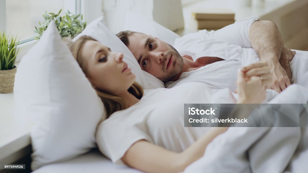 Closeup of couple with relationship problems having emotional conversation while lying in bed at home Closeup of couple with relationship problems having emotional conversation while lying in bedroom at home Couple - Relationship Stock Photo