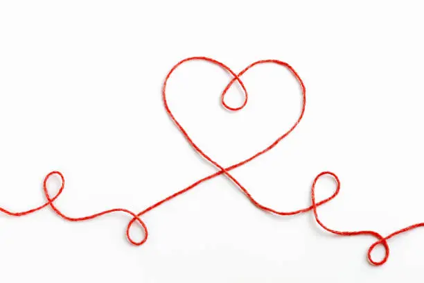 Photo of Red woolen thread in the shape of heart on white background
