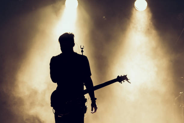 Rock band performs on stage. Guitarist plays solo. silhouette of guitar player in action on stage behind lights. stock photo