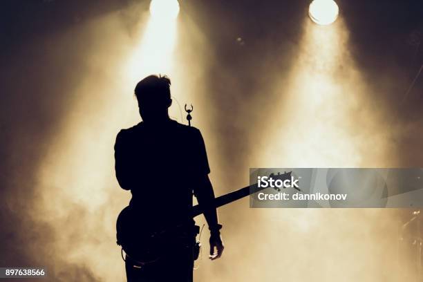 Rock Band Performs On Stage Guitarist Plays Solo Silhouette Of Guitar Player In Action On Stage Behind Lights Stock Photo - Download Image Now