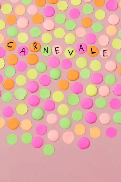 Hand written the word in Italian language Carnevale in each colorful confetti. Warm colors: pink, yellow and orange. Carnival party background concept, space for text. Overhead, flat lay, vertical orientation.