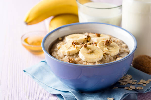 gachas de avena con plátano, nueces y miel en un tazón sobre fondo púrpura de madera. desayuno saludable. - porridge fotografías e imágenes de stock