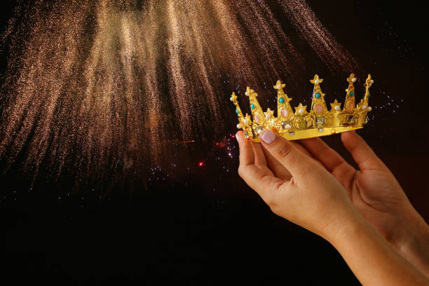 istock Woman's hand holding a crown for show victory or winning first place over black background with glitter overlay. 897671380