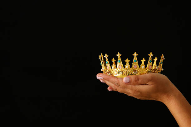 istock Woman's hand holding a crown for show victory or winning first place over black background. 897671424