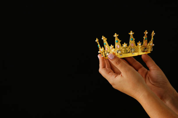 istock Woman's hand holding a crown for show victory or winning first place over black background. 897671440