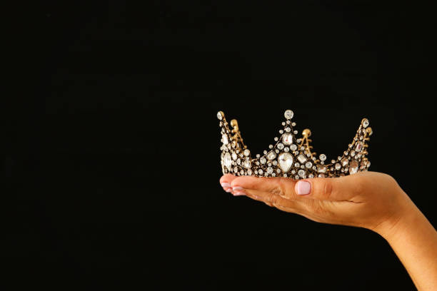 istock Woman's hand holding a crown for show victory or winning first place over black background. 897671796