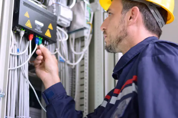 Engineer inspecting cabling connection in electrical room.