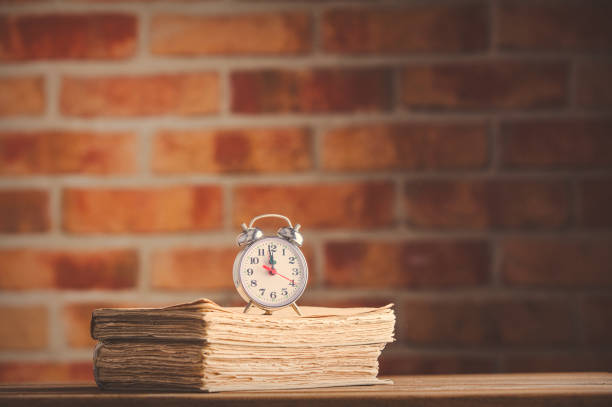 vintage alarm clock and old books on wooden table at brick wall background. Library