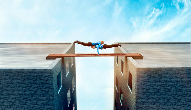 Concept of trust and and teamwork between two businessmen on rooftop Two acrobatic businessmen support each other while keeping the balance on a plank between two buildings. Concept of teamwork and trust in each other while the stakes are high. high fidelity stock pictures, royalty-free photos & images