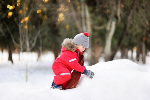 istock Little boy in red winter clothes having fun with fresh snow 897720552