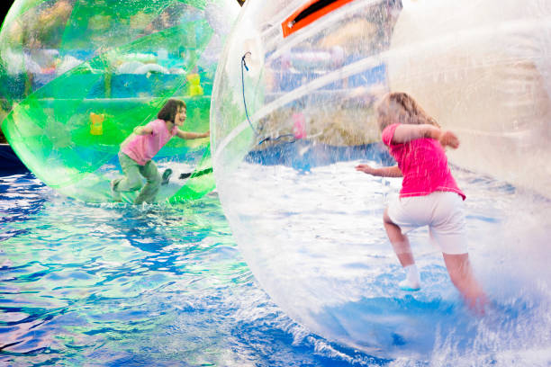 Girls Run in Floating Balls Two young girls playing inside a floating water walking ball. zorb ball stock pictures, royalty-free photos & images