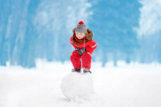 istock Little boy in red winter clothes having fun with snowball 897726378