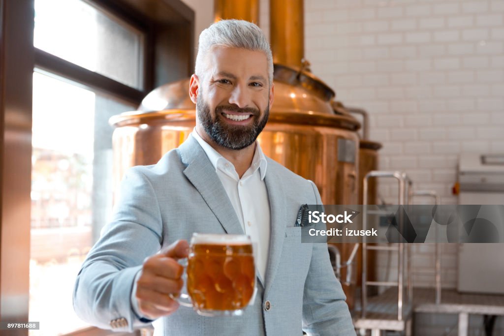 Handsome businessman holding a beer mug in microbrewery Portrait of handsome businessman holding a beer mug in microbrewery. Brewery owner with a glass of fresh beer. Adult Stock Photo
