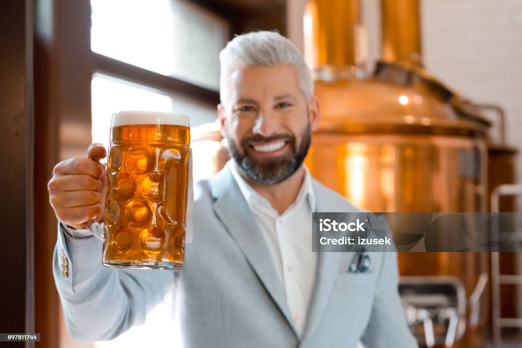 Handsome businessman holding a beer mug at brewery Handsome businessman holding a beer mug at brewery. Brewery owner with a glass of fresh beer. Adult Stock Photo