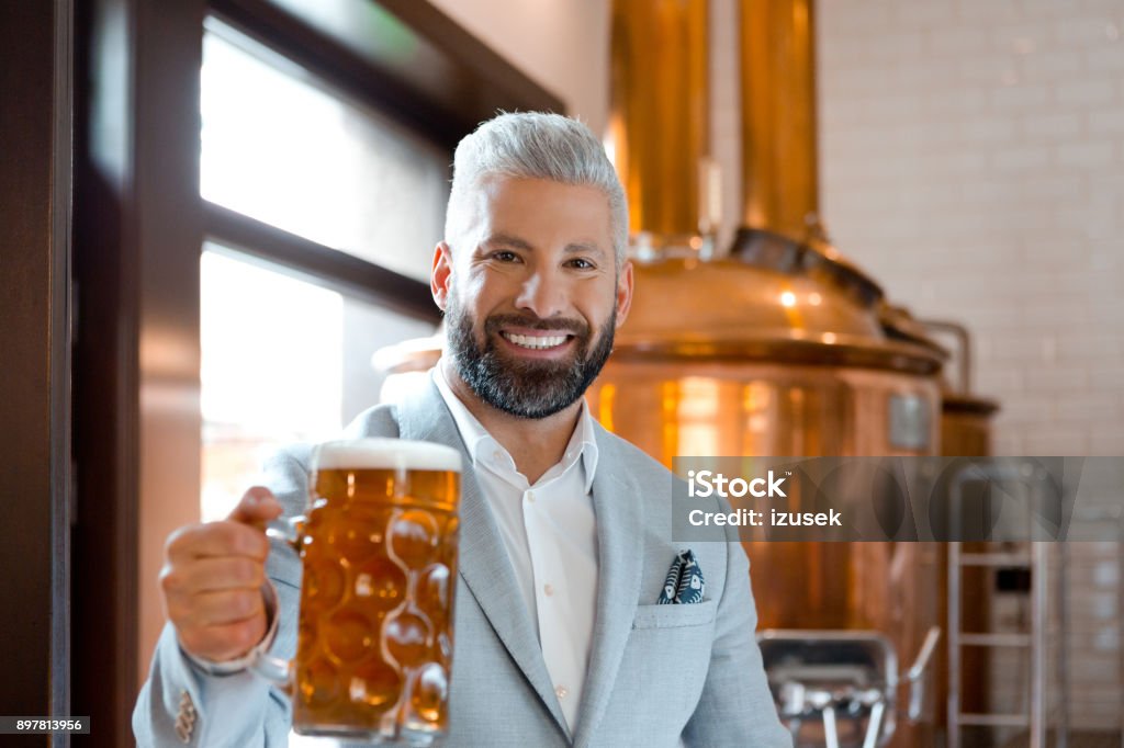 Micro brewery owner with a mug of fresh beer Elegant microbrewery owner with a mug of beer in his pub. Handsome brewery owner with a glass of fresh beer. Adult Stock Photo