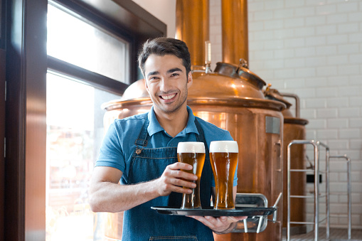 Portrait of smiling waiter holding a tray with glasses of beer in brewery