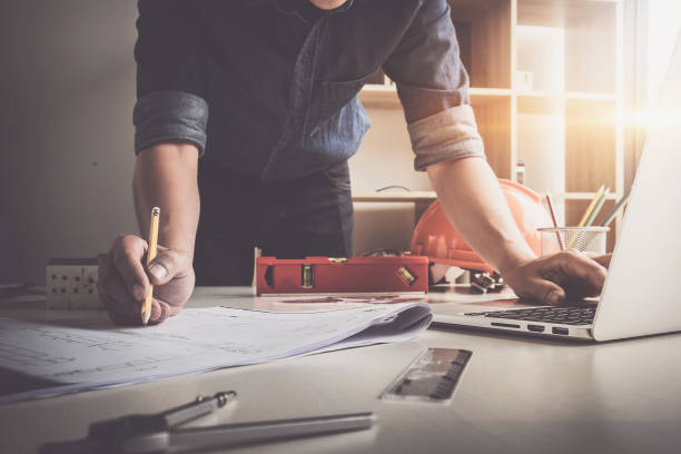 istock Architect man holding pencil working with laptop and blueprints for architectural plan, engineer sketching a construction project concept. 897853202