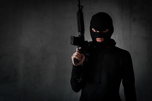 Robber,thieve or terrorist with gun and masked for  attack with assault rifle black suit ready shooting,aiming on copy space background violence concept