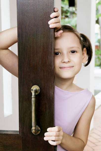 Smiling little girl in violet dress looking out of open door in scandinavian style house stock photo