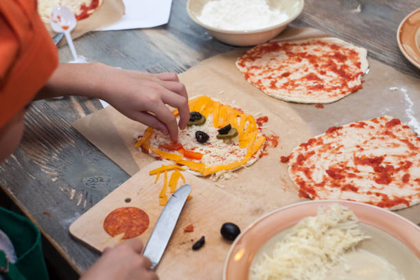 halloween party ideas for kids ghost pizza with cheese and olives. baby hands decorate festive pizza - pizza sauces chef making imagens e fotografias de stock