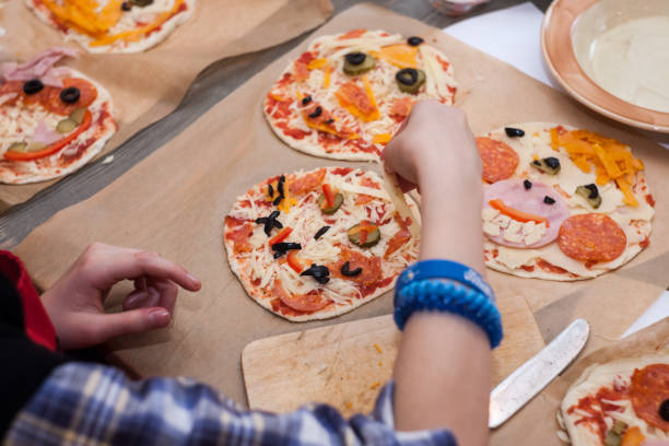 子供のためのハロウィーン パーティーのアイデアはゴースト チーズとオリーブのピザです。赤ちゃんの手を飾るお祝いピザ - cheese making ストックフォトと画像