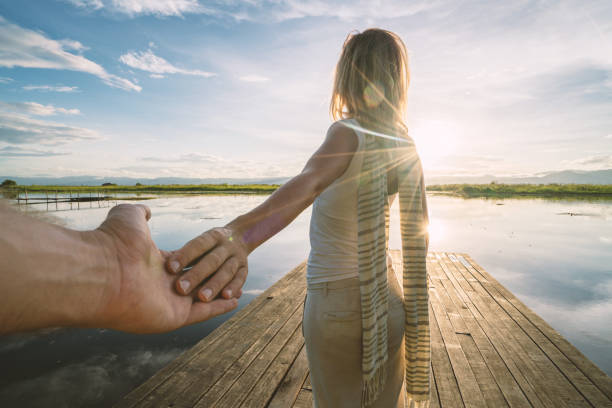 Follow me concept - Young woman traveling leading boyfriend on wooden lake pier. Inle lake, Myanmar, Asia