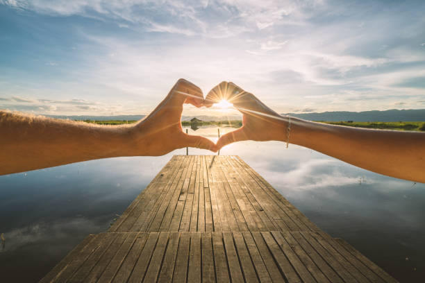 Close up on couple's hands making heart shape frame on lake at sunrise, shot at Inle lake on wooden pier, Myanmar, Asia
