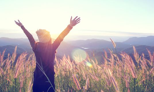 Happy Woman Enjoying Nature on grass meadow on top of mountain cliff with sunrise. Beauty Girl Outdoor. Freedom concept. Len flare effect. Sunbeams. Enjoyment.