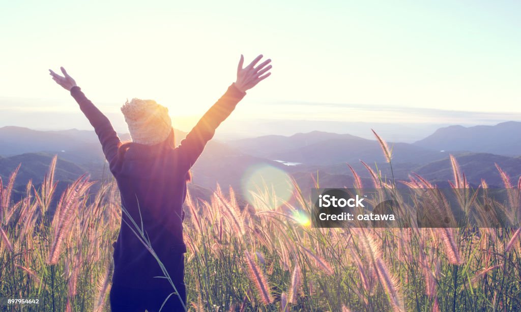 Happy Woman Enjoying Nature on meadow on top of mountain with sunrise. Outdoor. Freedom concept. Happy Woman Enjoying Nature on grass meadow on top of mountain cliff with sunrise. Beauty Girl Outdoor. Freedom concept. Len flare effect. Sunbeams. Enjoyment. Happiness Stock Photo