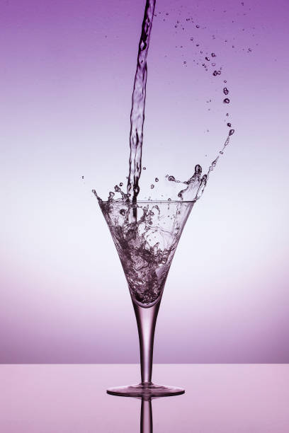 istock Water fall into a glass and splash on a bright purple background 897958252